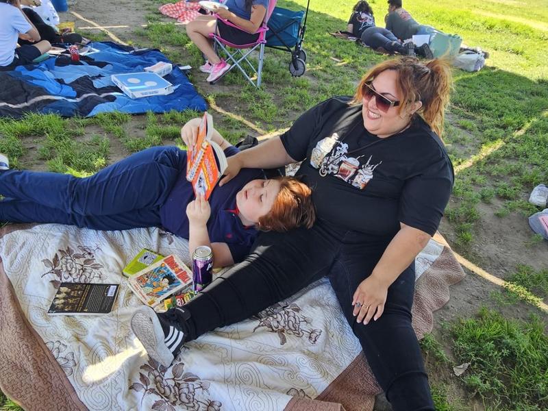 A woman and a child reading books while sitting on a blanket outdoors.
