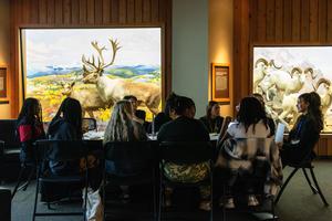Students discuss around a table with a museum exhibit as backdrop