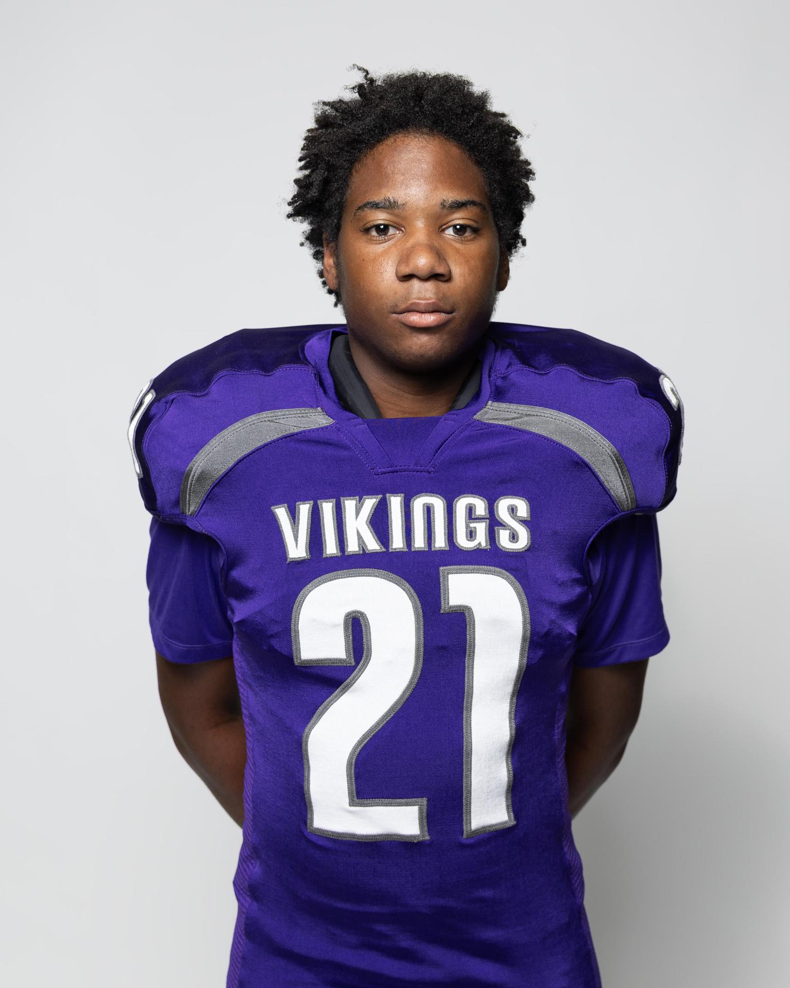 Youth in a purple Vikings football jersey stands upright with a serious expression.