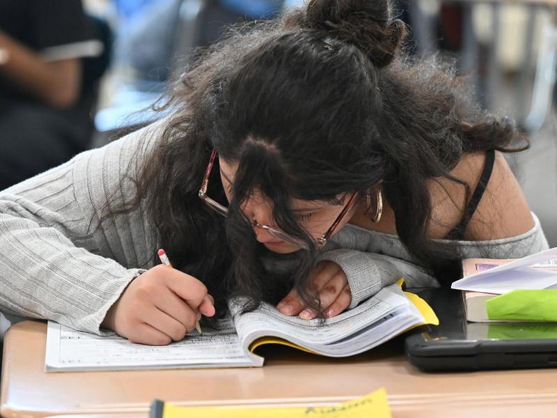 A student focused on writing in a notebook at a desk.