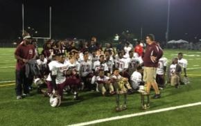 A youth football team poses together holding trophies on a night field.