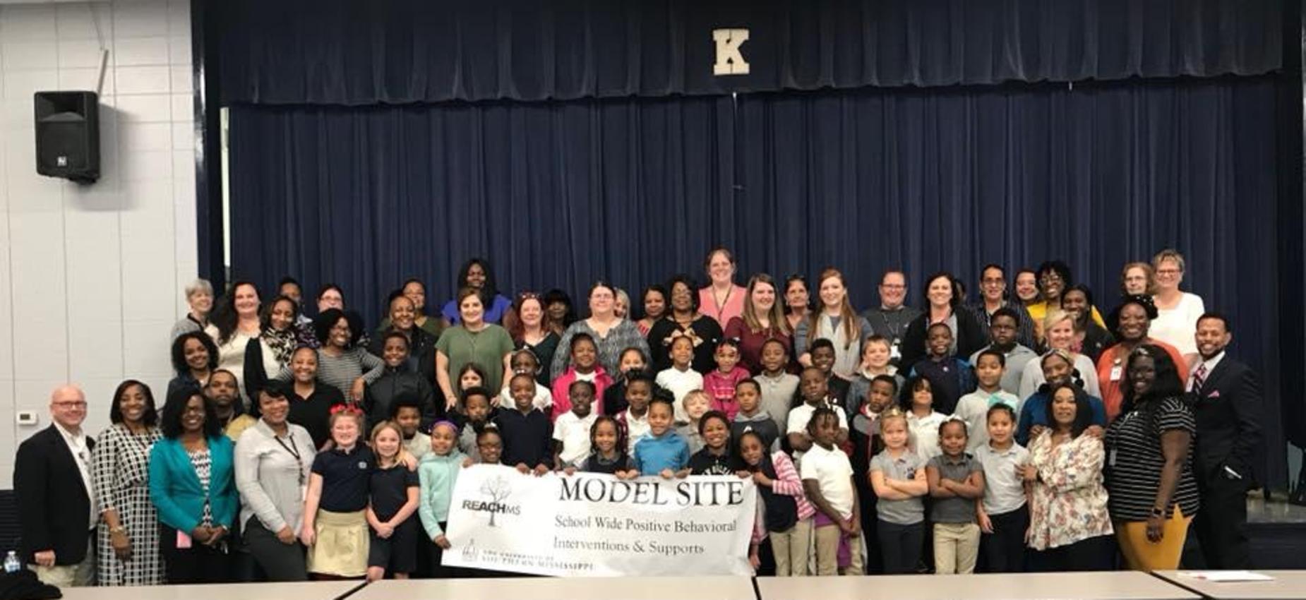 students and staff with model school sign