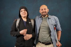 Two men standing together, one with a hooded jacket and the other with a cane.
