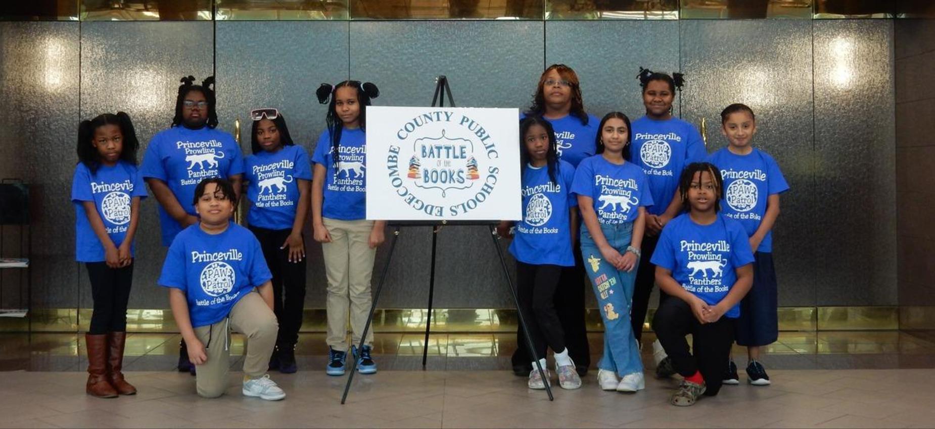 Princeville students and adults in blue school shirts pose beside an Edgecombe County Public Schools Battle of the Books sign.