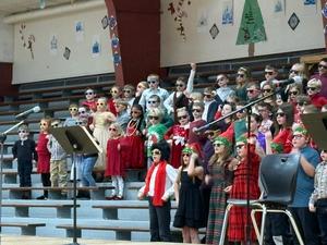 Students in sunglasses and holiday accessories perform together on stage, showcasing their enthusiasm.