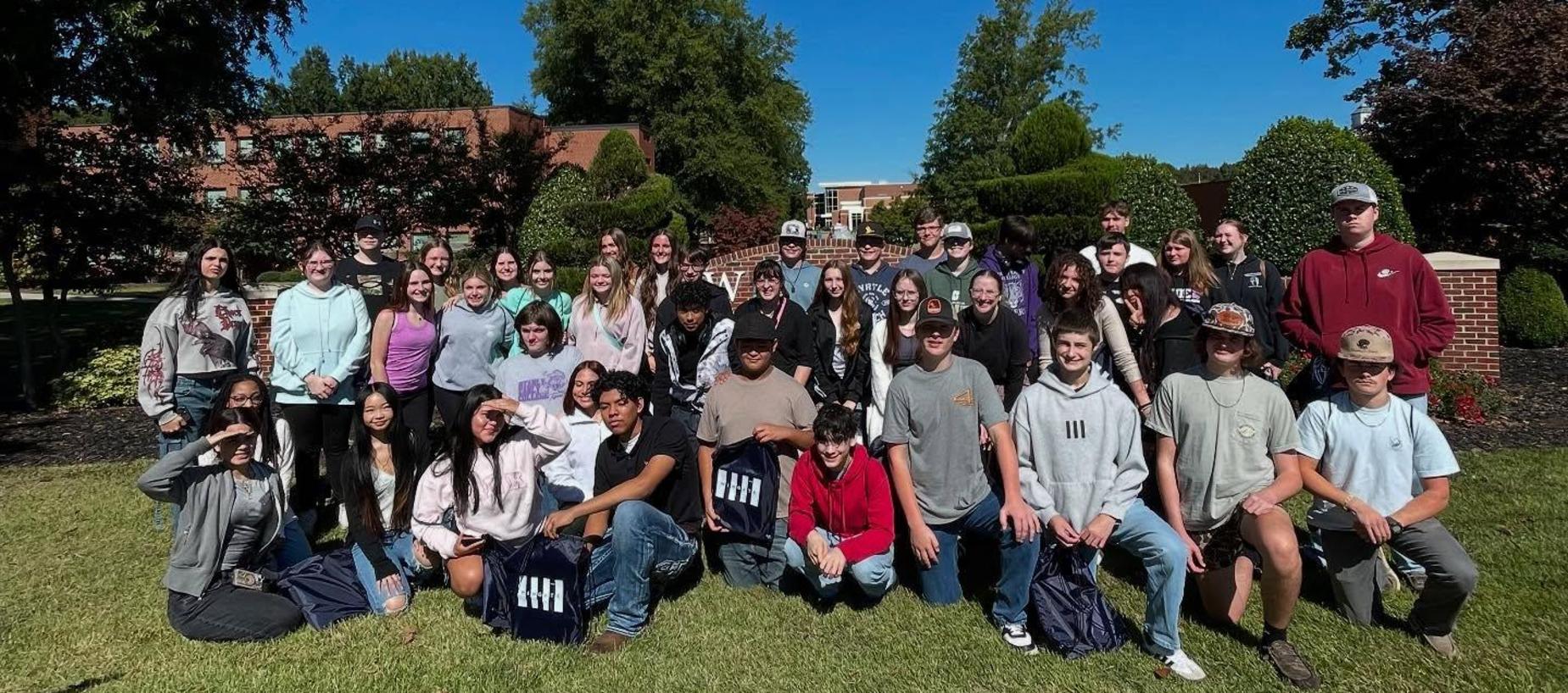 Group of students posing outdoor in front of a building and trees.