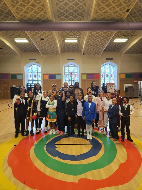 Scholars and visitors stand in front of the Mandela logo in the school gym