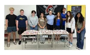 Group of students standing behind tables filled with snacks.