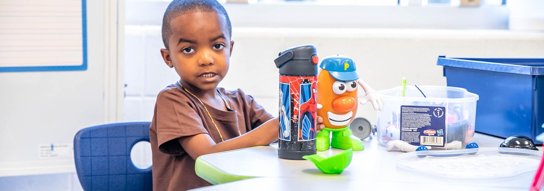 A boy playing with a toy on a table in a bright classroom.