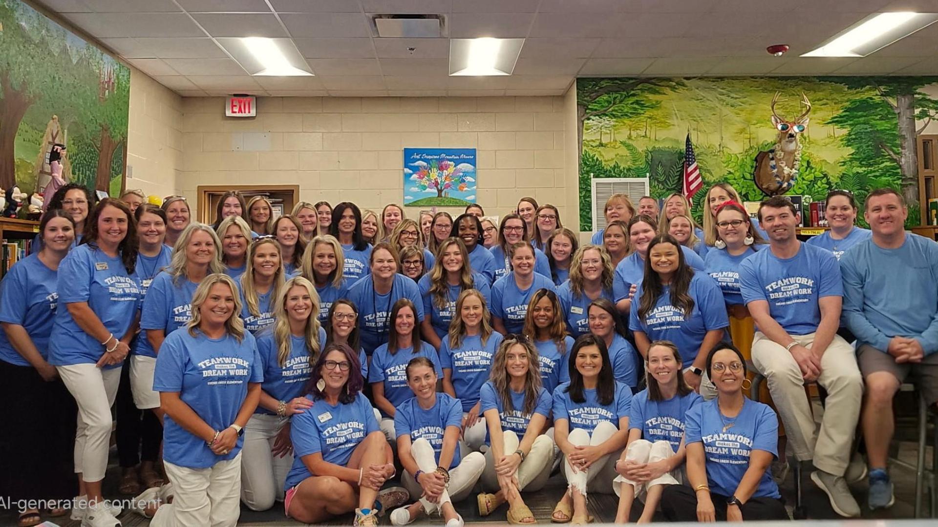A large group of smiling educators in blue shirts sitting in a library setting.