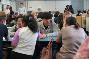 A busy cafeteria scene with several groups of people engaged in conversation.
