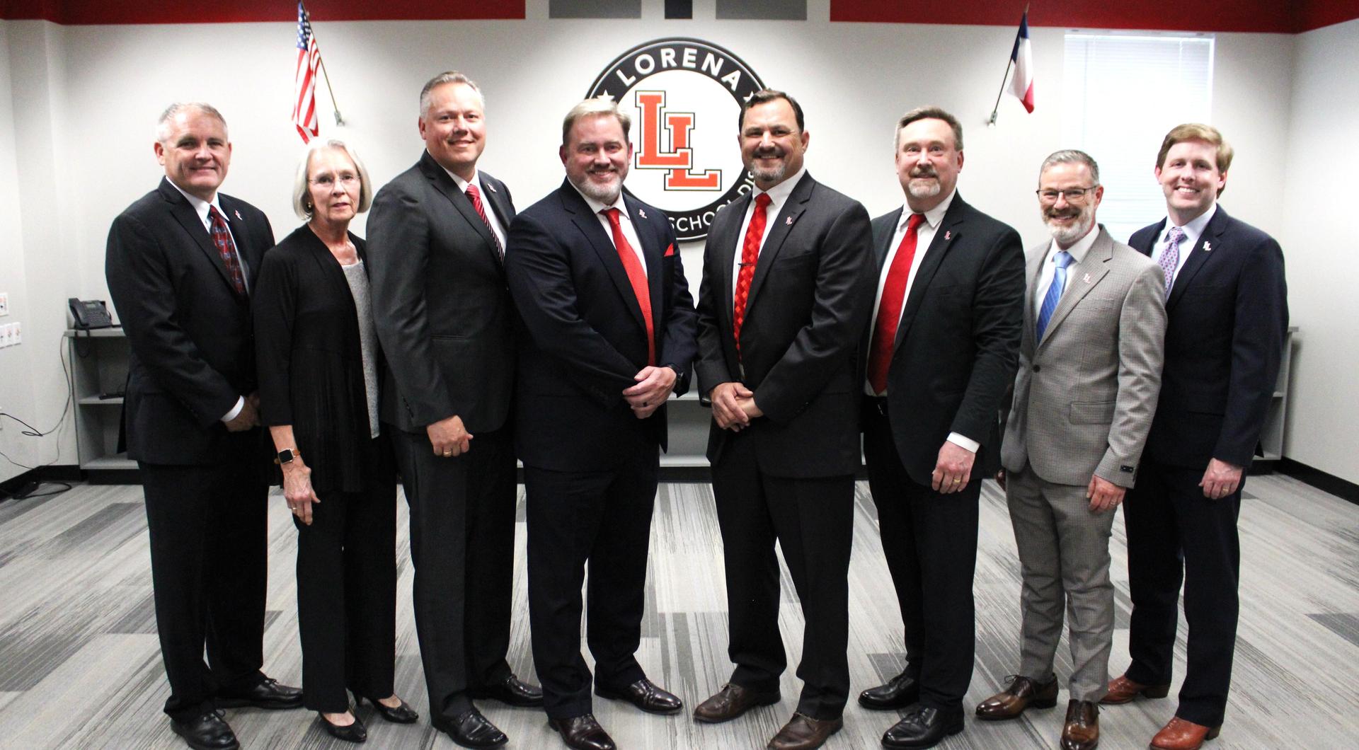 Lorena ISD School board members in front of black LISD circle logo with red LL in the middle