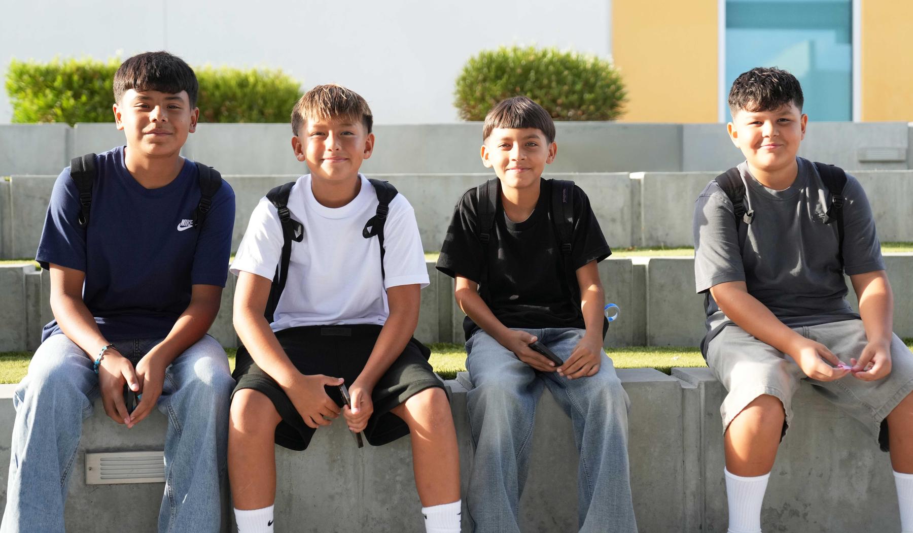 four boys sitting on a cement bench
