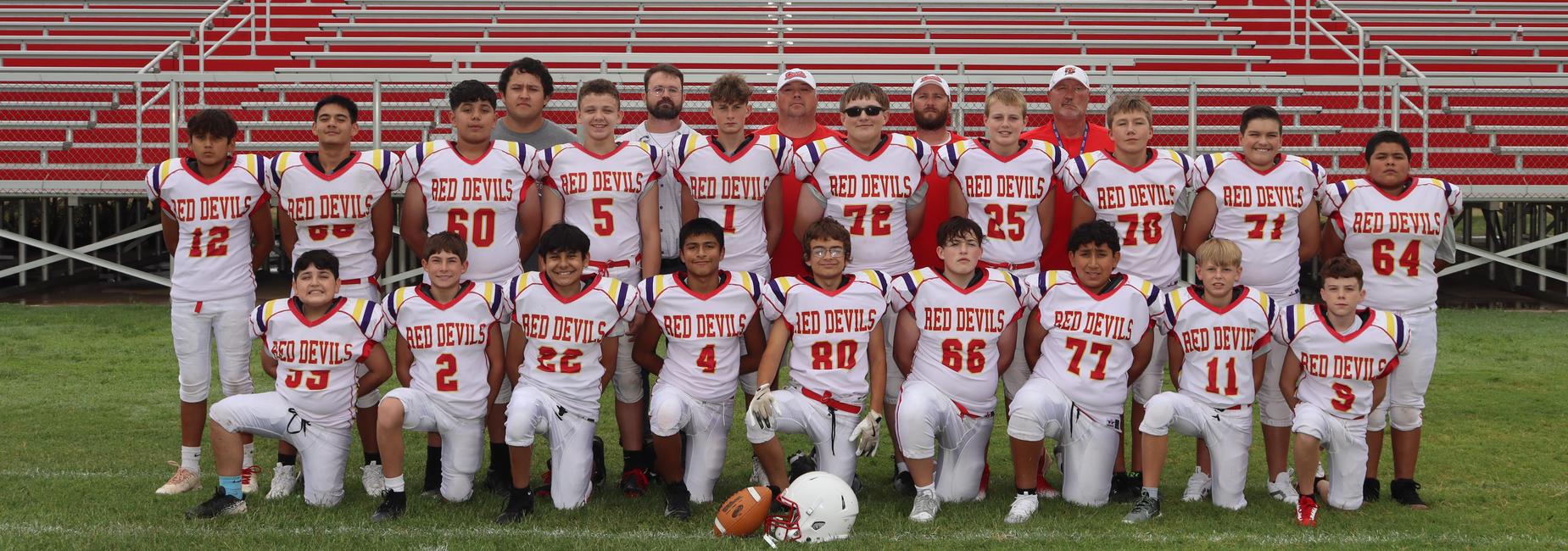 Football team poses in uniforms in front of bleachers.