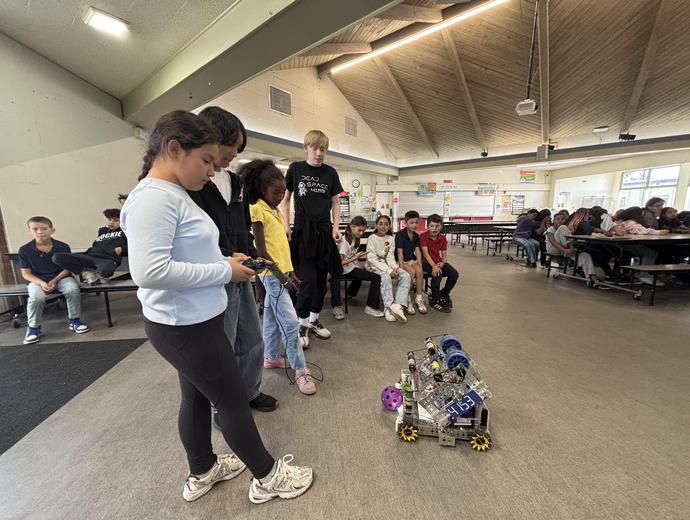 Students observing a small robot being operated in a school cafeteria.