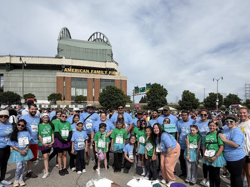 A large group of people in blue and green shirts gathered outside a stadium.
