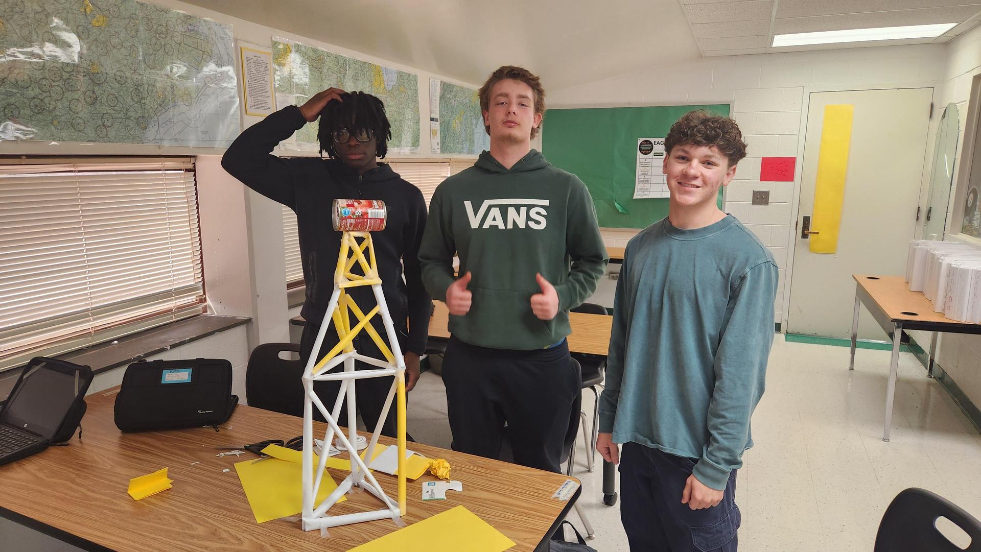 Three students posing with a tower model made from craft materials.