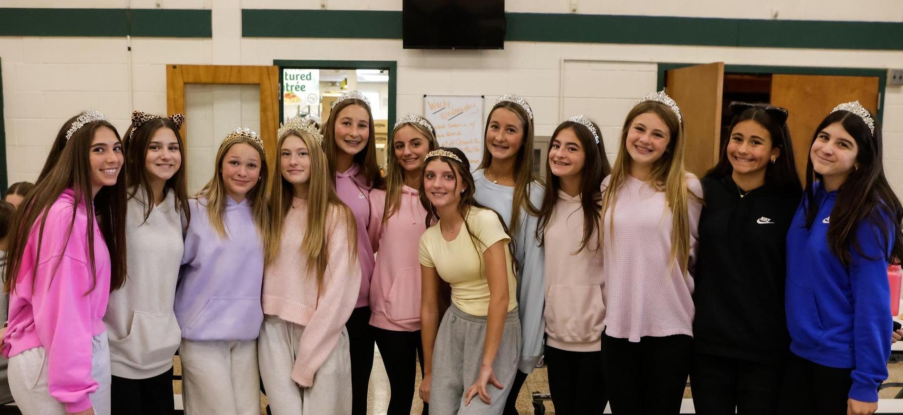 A group of cheerful teens wearing tiaras, gathered at a cafeteria table.