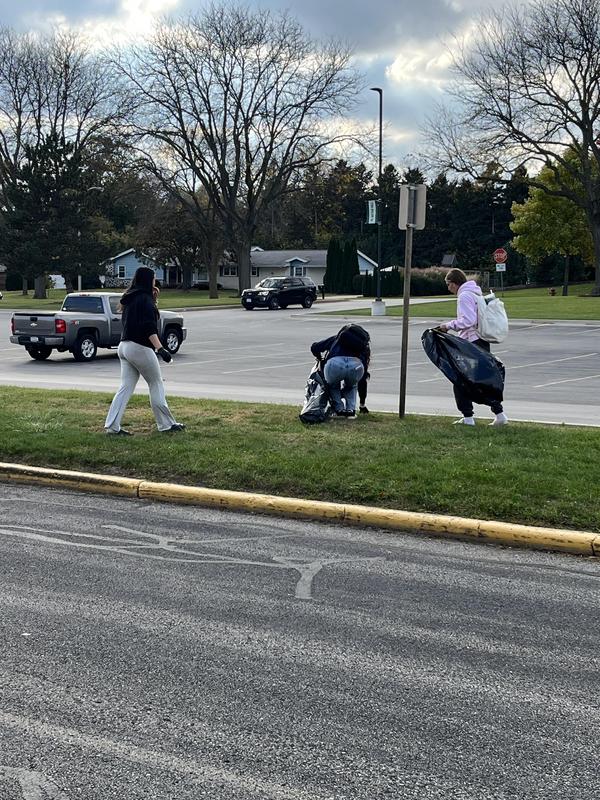 Three people cleaning up trash along a roadside with black garbage bags.