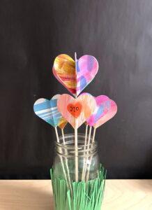 Colorful paper hearts on sticks arranged in a jar with green grass.