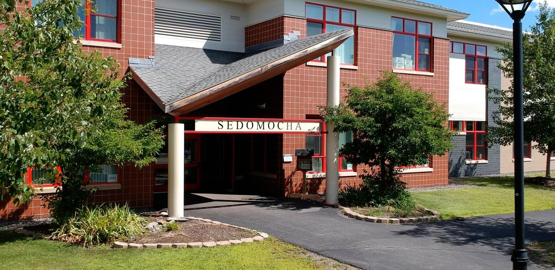 Sedomocha school building with red-trimmed windows and green landscaping.