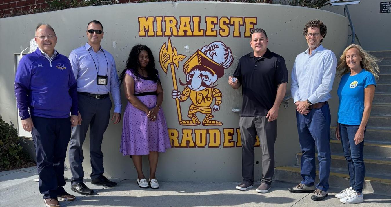 Group of six people standing in front of a mural at a school.