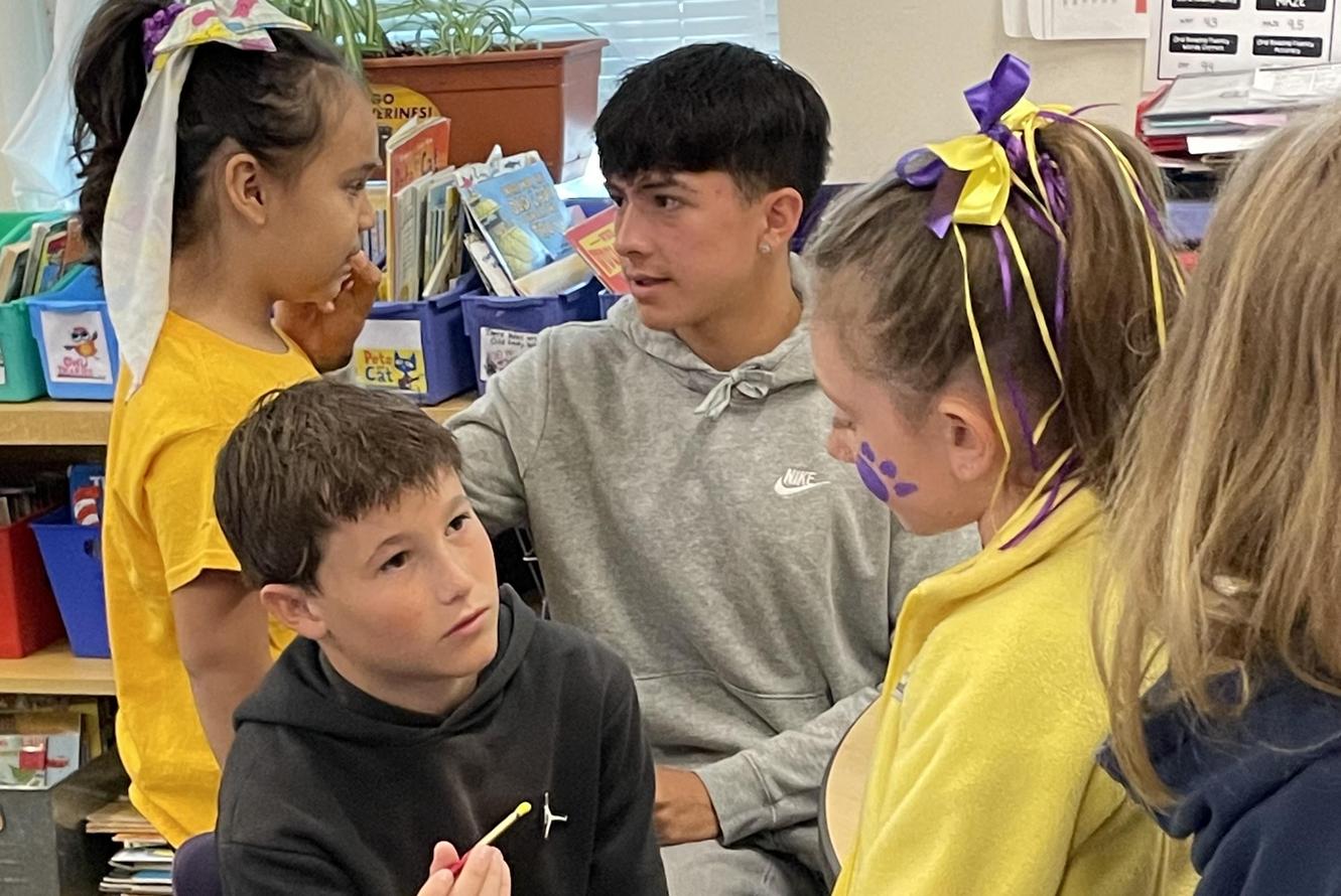 Students engaged in a classroom art activity, with one boy painting a girl's face.