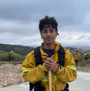 A student outside with a shovel wearing fire fighting safety gear.