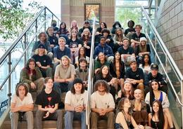A diverse group of students sitting on stairs, smiling for the camera.