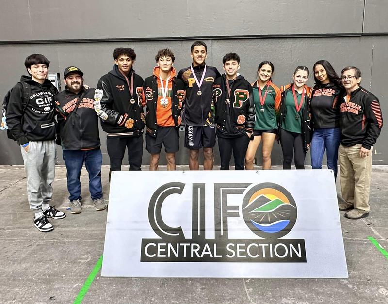 A group of student-athletes and coaches from Porterville and Monache High Schools pose proudly behind a CIF Central Section banner. Several wrestlers wear medals around their necks, celebrating their achievements at the Masters Championships. The group includes both male and female wrestlers along with coaching staff, all smiling for the photo.