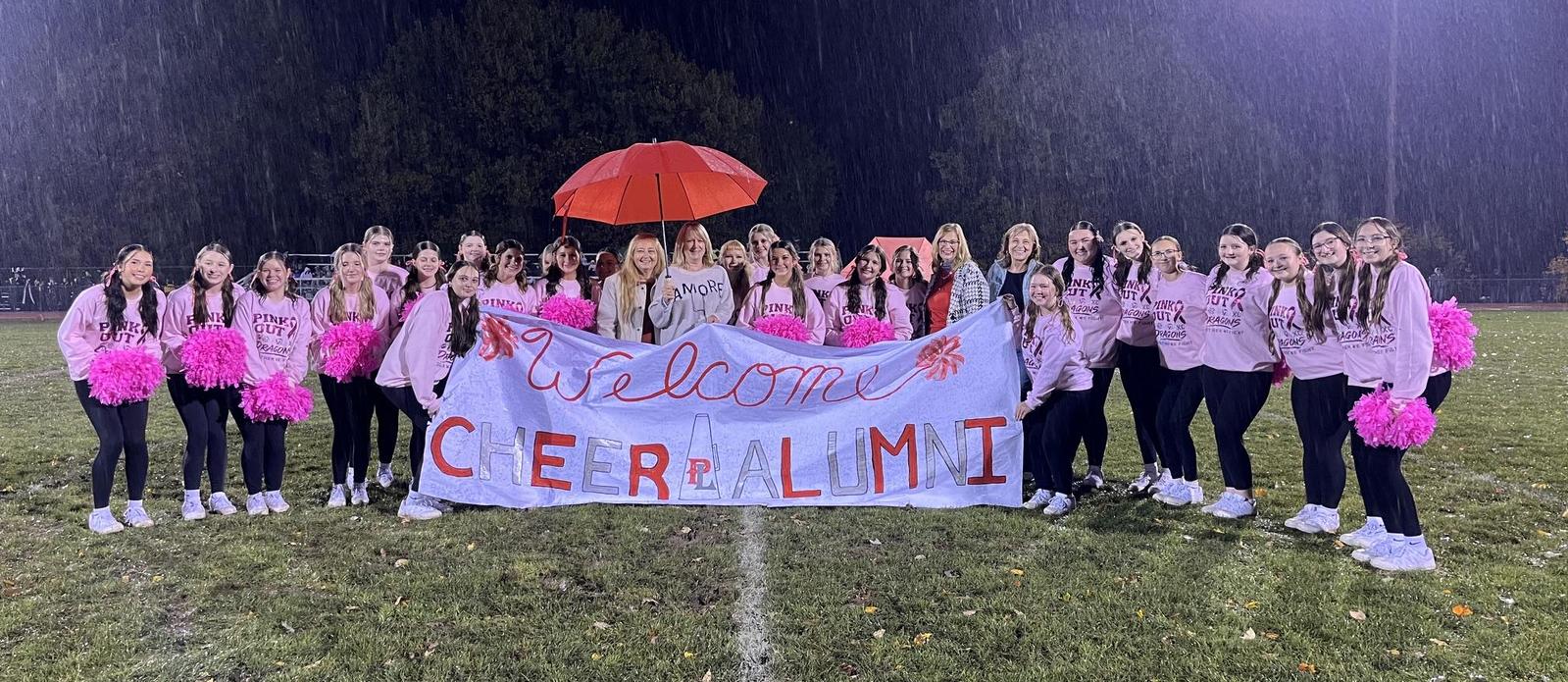 Alumni Night Cheerleader recognition with four alumni and the current squad holding a welcome back sign.