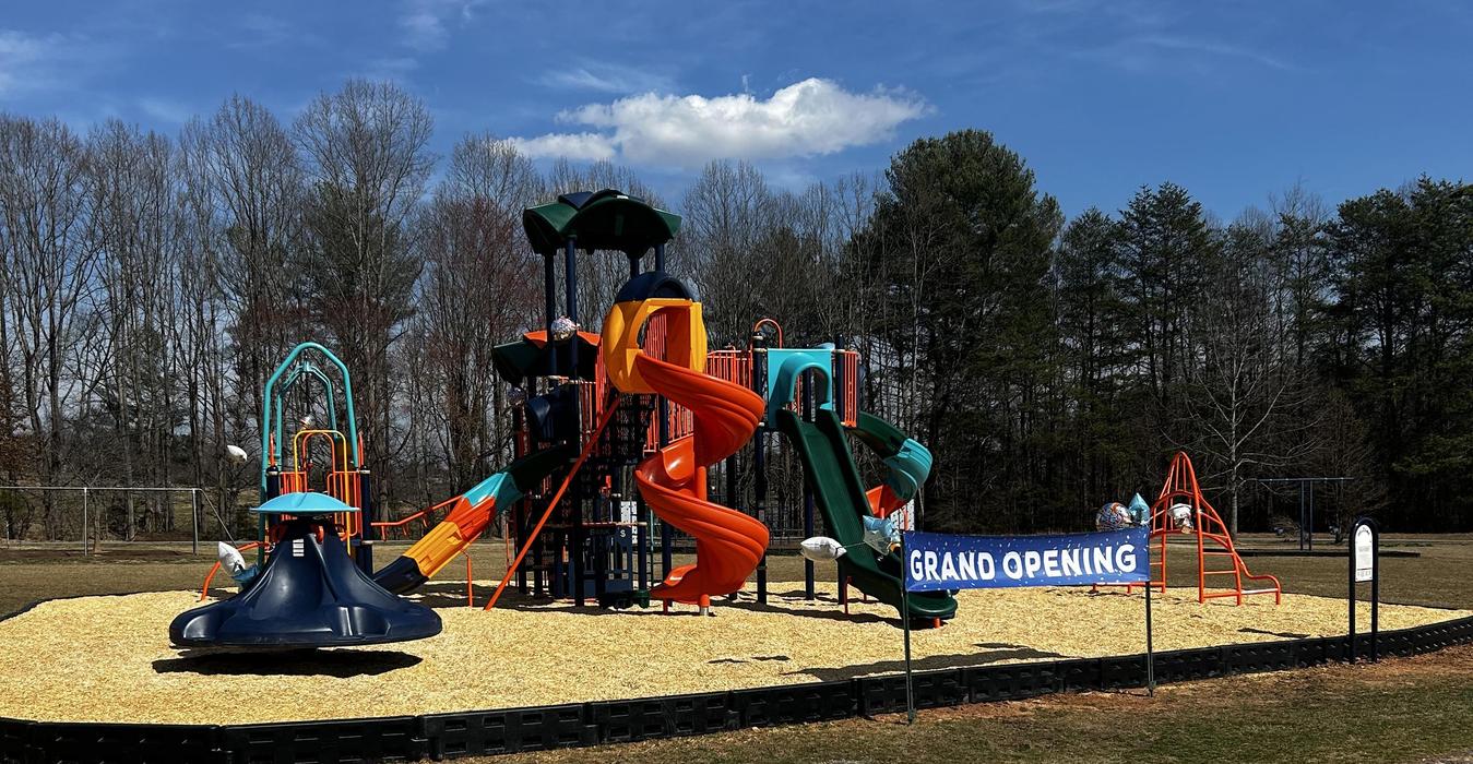 Colorful playground with a banner for a grand opening in a park.