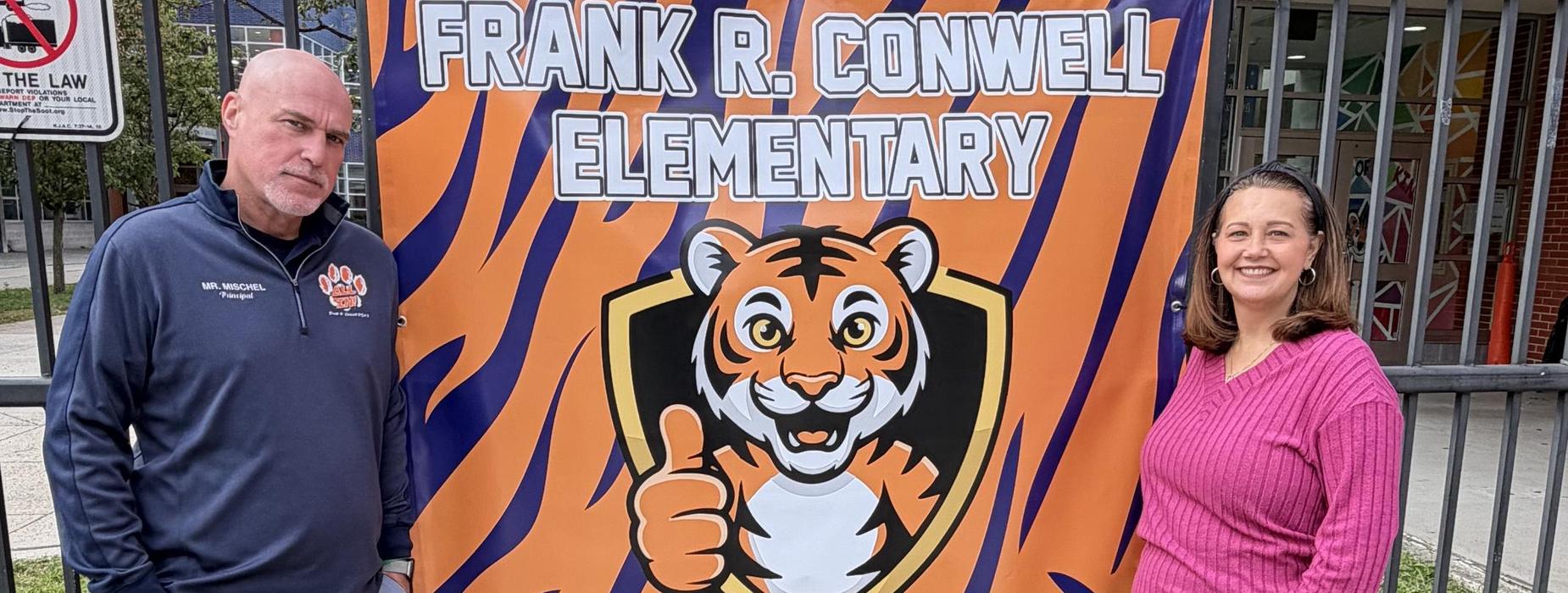 Two people standing beside a colorful school banner featuring a tiger mascot.