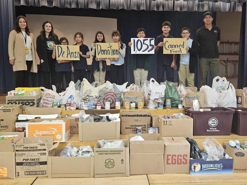 Students and adults display food donation signs in front of collected canned goods.