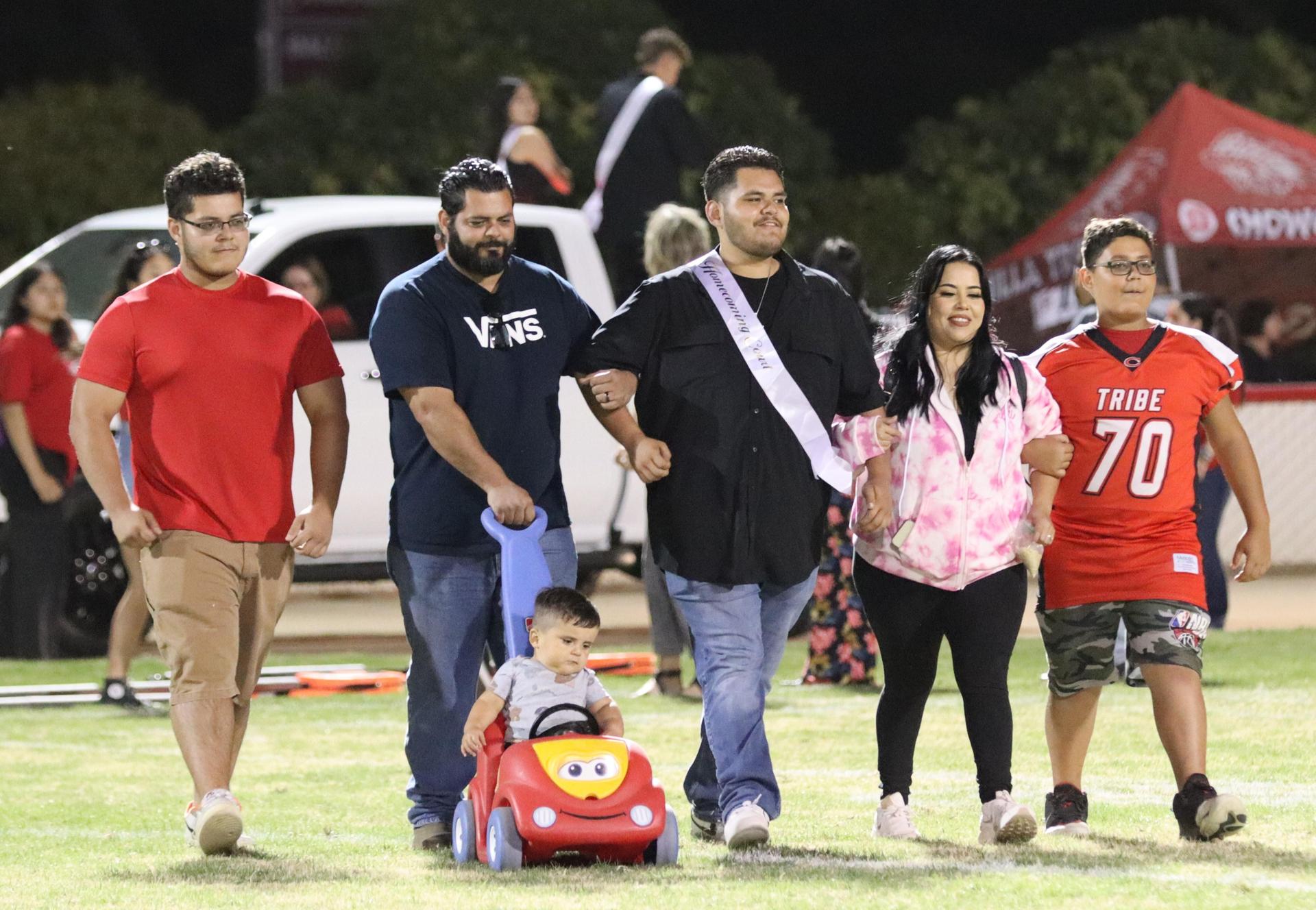 homecoming king and queen candidates walking across the field with their escorts
