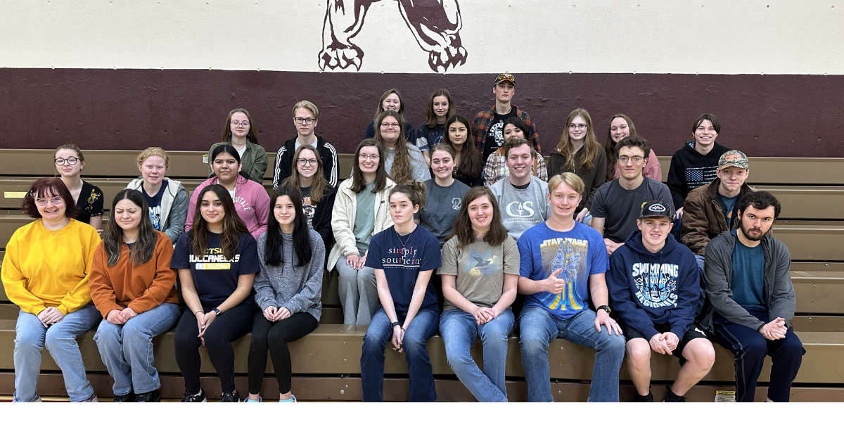 Group photo of students posing together on bleachers in a gymnasium.