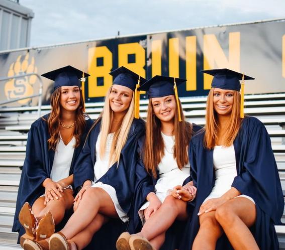 4 teen girls wearing graduation cap and gowns sitting on bleachers