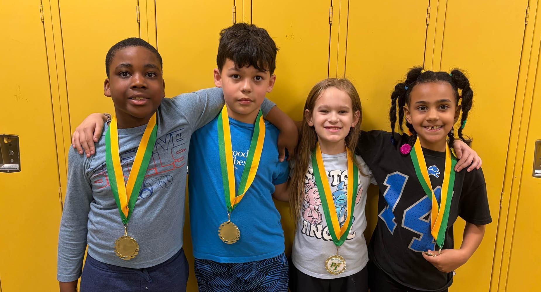 Four students wearing medals around their necks stand in front of bright yellow lockers