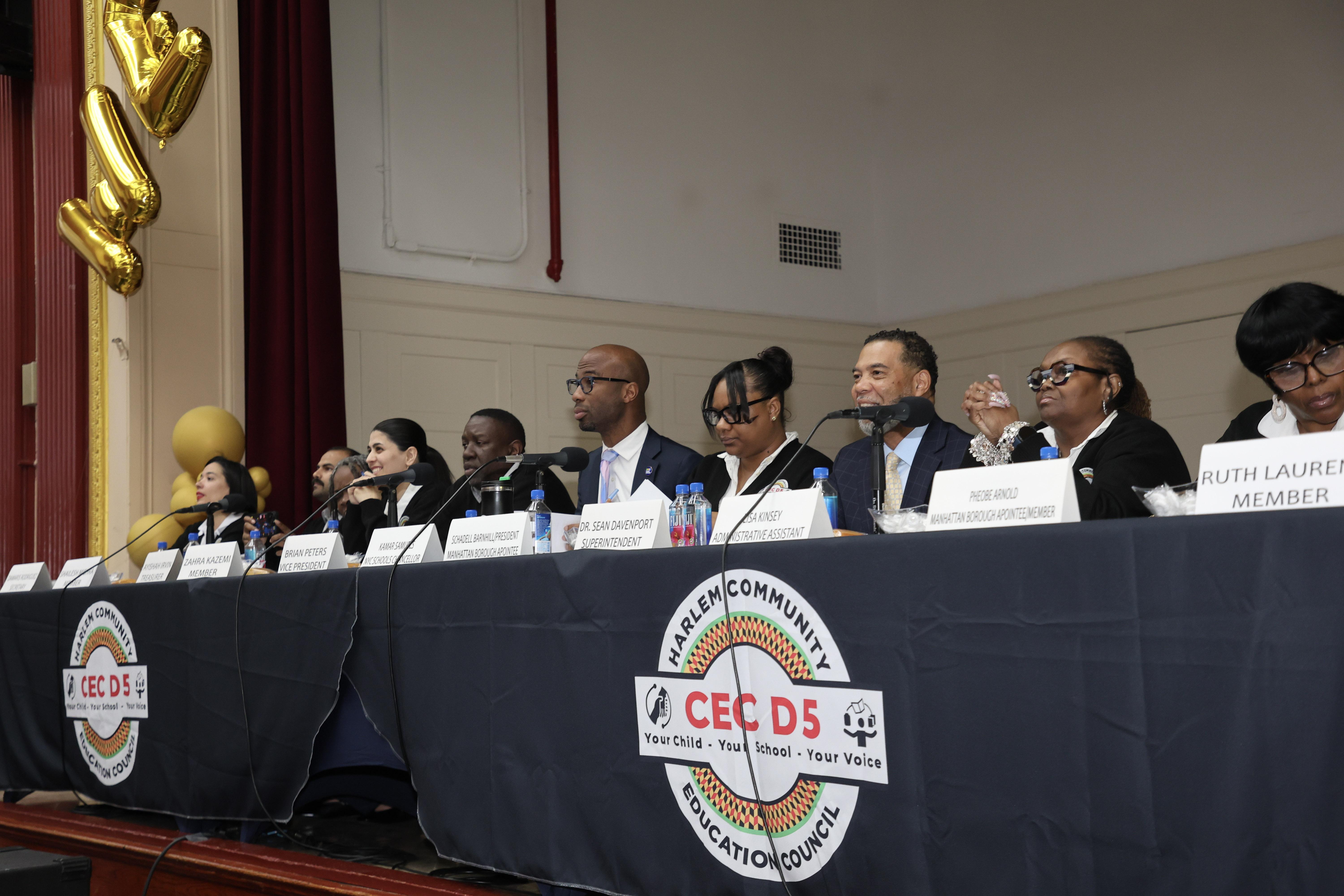 Forum with participants seated at a long table, discussing education topics.