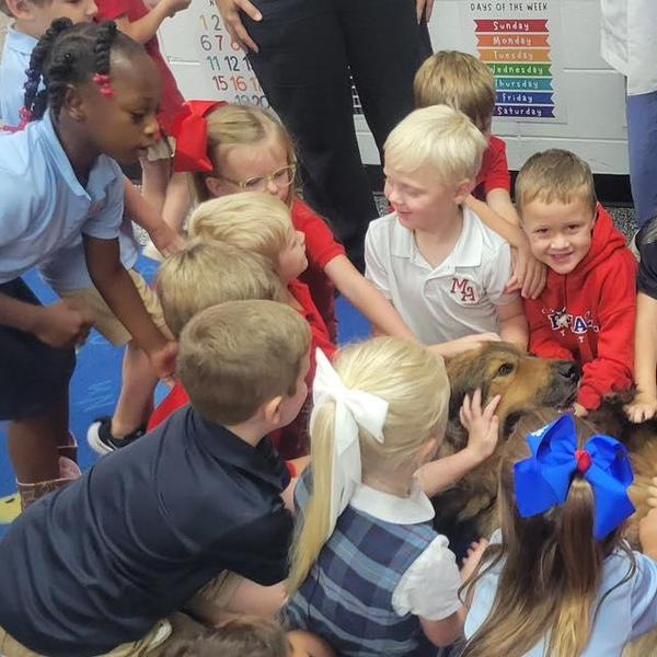 Children gathered around a friendly dog in a classroom setting.