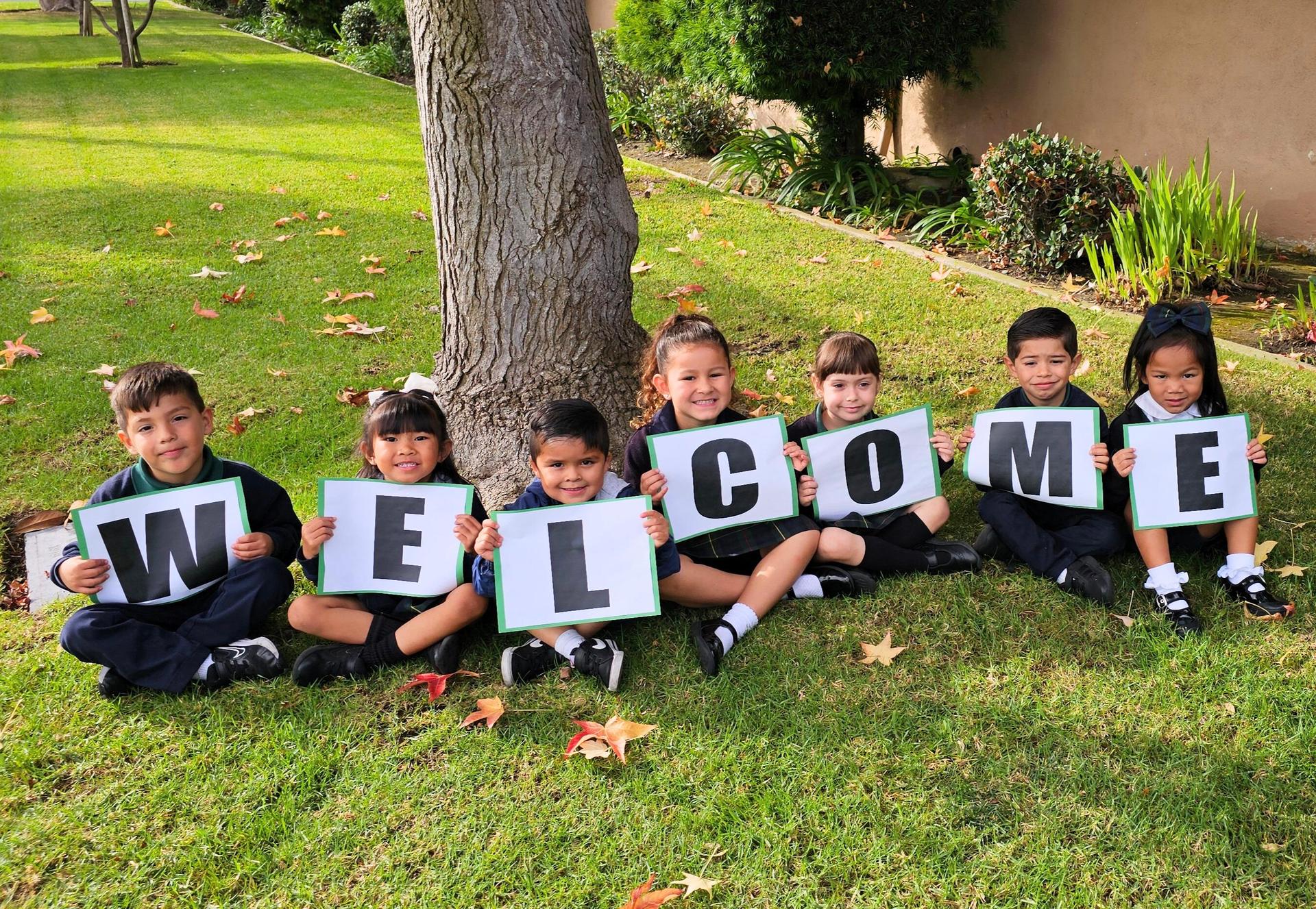 TK class under a tree with a sign that says welcome