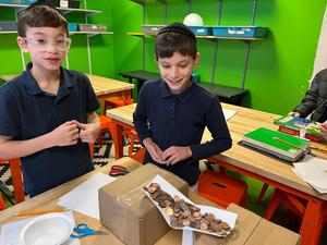 two fourth grade boys test the strength of their bridge with pennies.