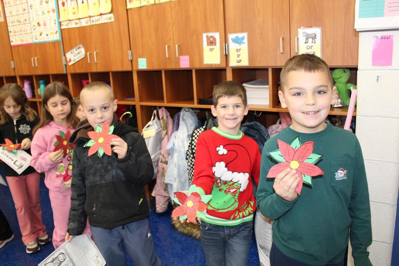 three boys smile holding poinsettia craft they made
