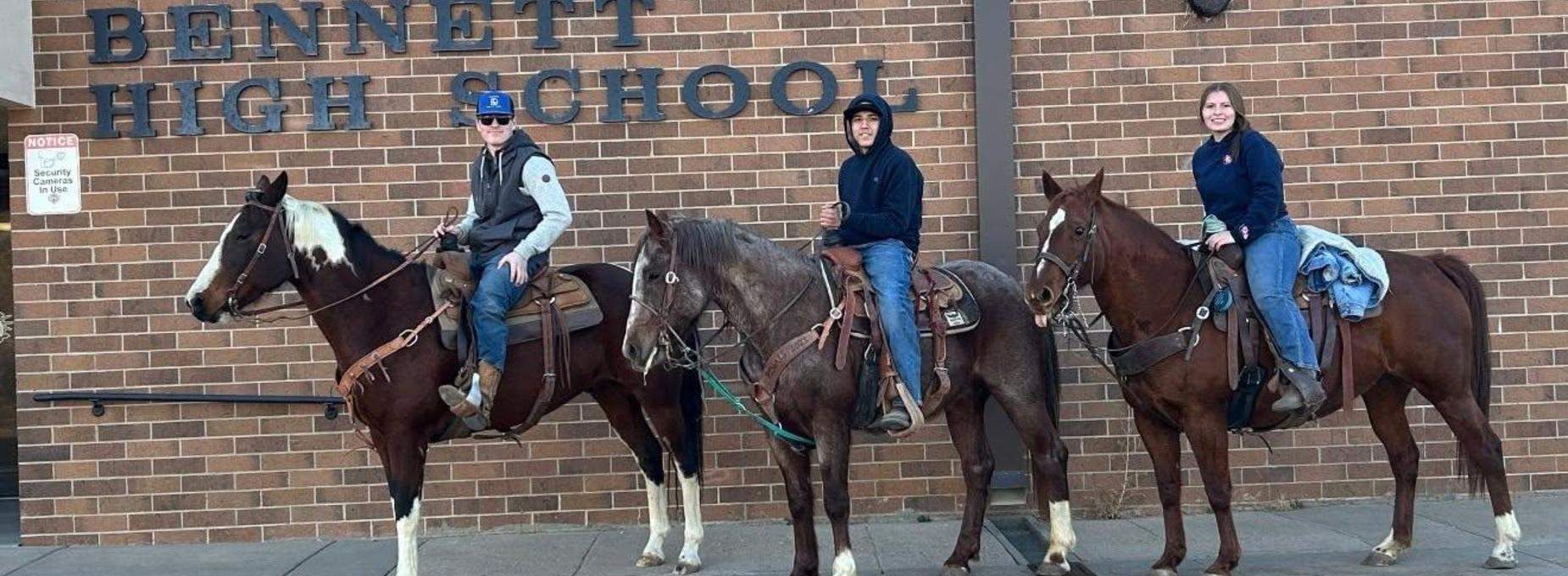 Three people on horseback in front of Bennett High School.