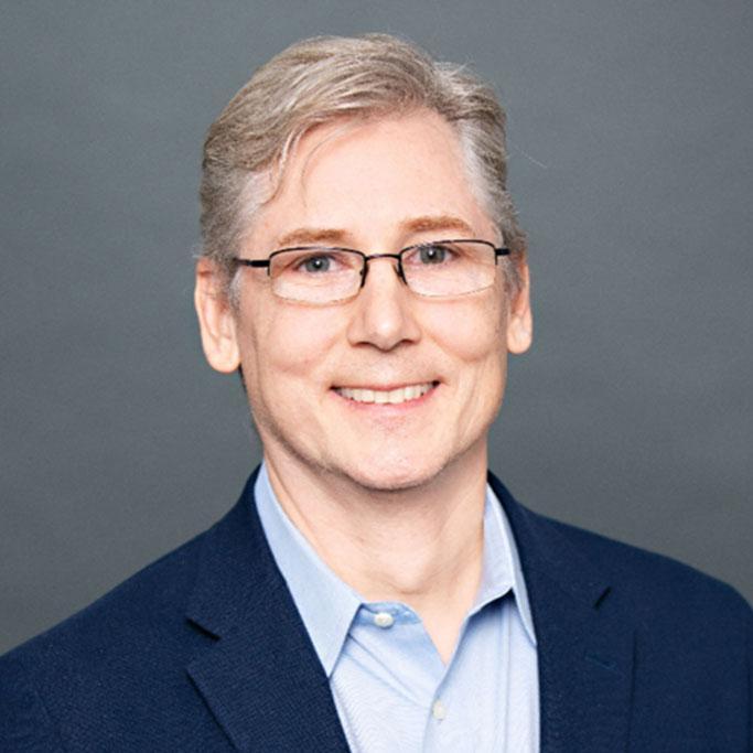 A smiling man with light gray hair and glasses