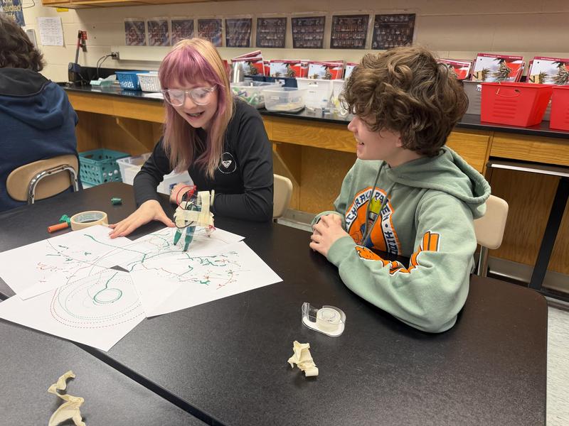 two students smiling as robot colors across paper