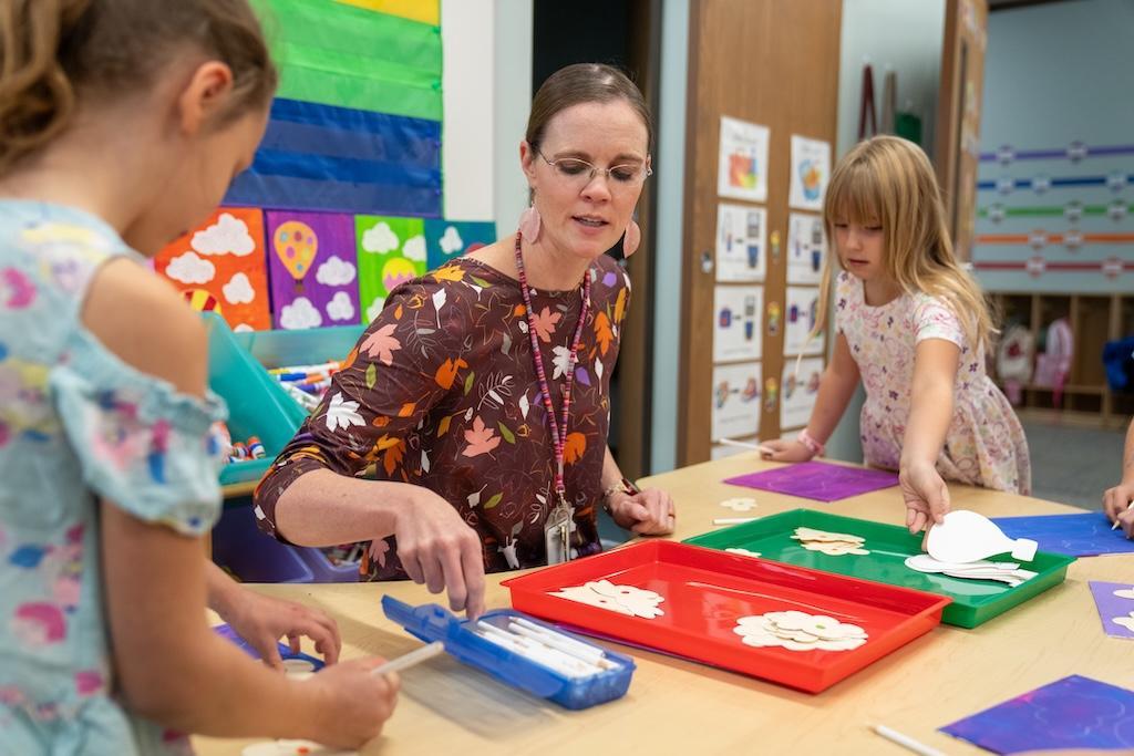teacher is sitting at a table working with two students in a school