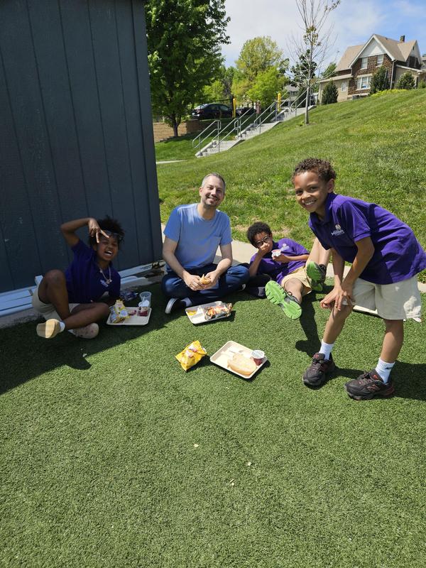 Scholars and teacher eating lunch on the soccer field