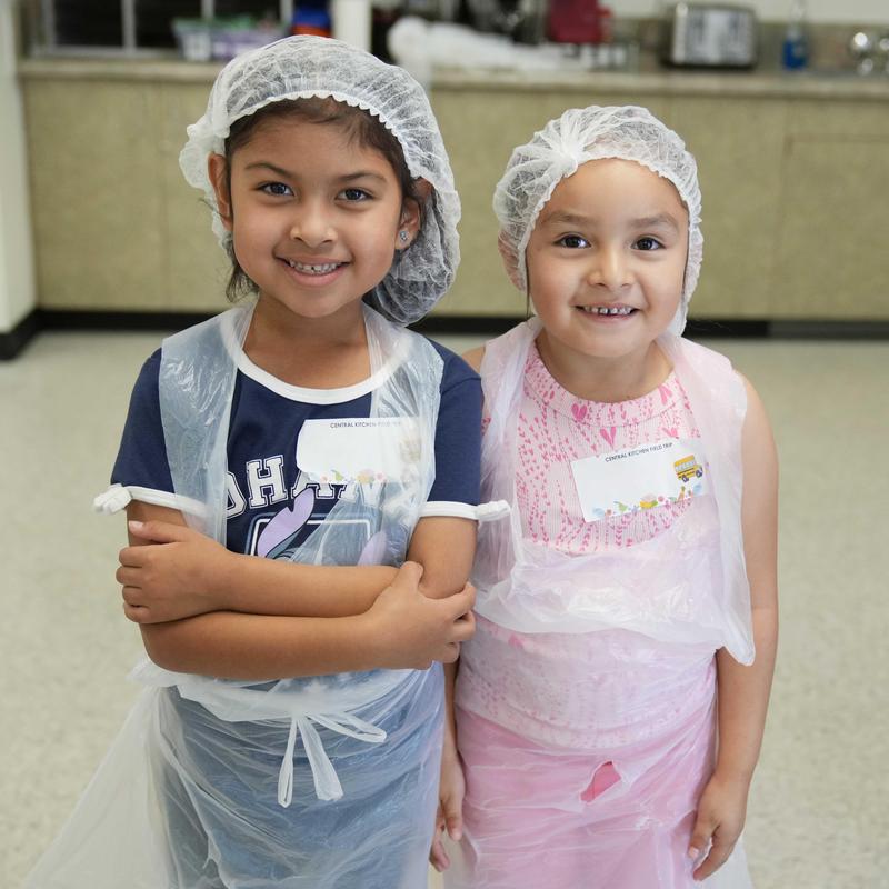 Two elementary girls with hair nets and apron during a visit to Central Kitchen