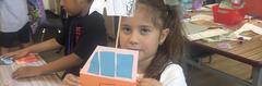 A girl holding a colorful model of a house with drawn details and cut-out windows.